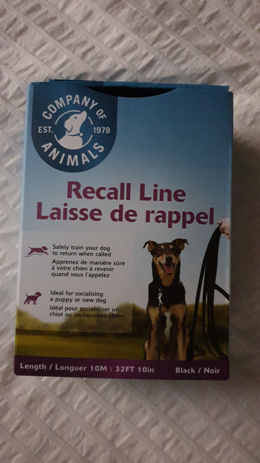 A vertical eye-level shot of the packaging for a 'Company of Animals' Recall Line. The blue and white box features a photo of a dog in a field and specifies a length of 10 metres (32 feet 10 inches) in black. The box is resting on a white textured fabric surface.