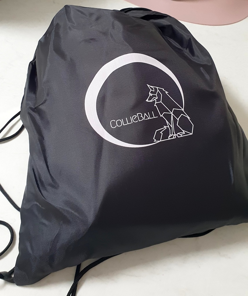A dark blue drawstring bag sits on a white marble-style countertop. The bag features a white geometric logo of a sitting dog inside a circle, with the word "COLLIEBALL" written in a modern, sans-serif font.