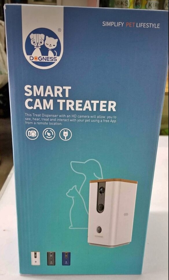 A vertical eye-level shot of the blue and teal retail packaging for a Dogness Smart Cam Treater. The box features a white and wood-top treat dispenser with an HD camera, along with the Dogness logo depicting a dog and a cat. The text on the box reads 'SIMPLIFY PET LIFESTYLE' and describes the device's ability to see, hear, treat, and interact with pets via a free app.