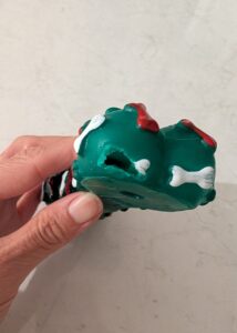 A hand holding the broken end of a cheap green rubber dog bone toy, showing a clean hole where a corner piece has easily been bitten off.