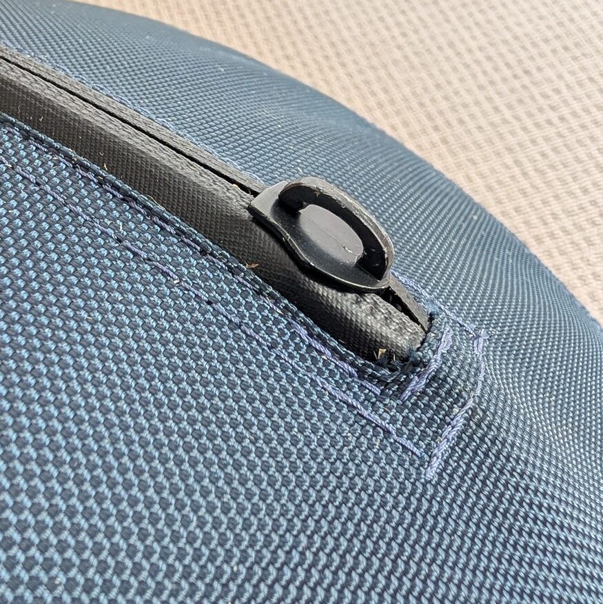 Angled top view of a blue durable textile herding ball showing the black metal zipper track end and exposed slider top sitting prominently above the stitched seam.