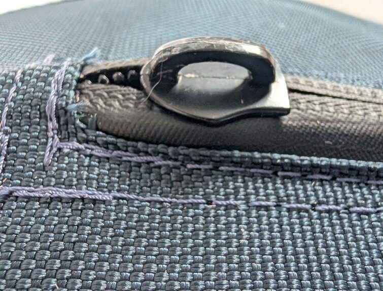 Macro close-up profile view of the exposed hard black metal zipper tab sitting above the protective neoprene lip of a blue canvas herding ball.