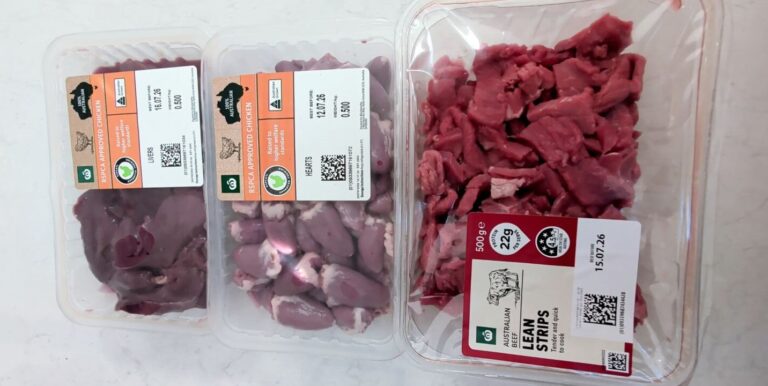 Three plastic supermarket packages of raw meat stacked on a counter, showing RSPCA Approved Chicken Livers, Chicken Hearts, and Australian Beef Lean Strips.