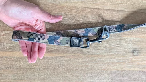 Hand holding the camo print Stylish Hound multi-function leash handle loop formed by clipping the end snap hook onto a D-ring.