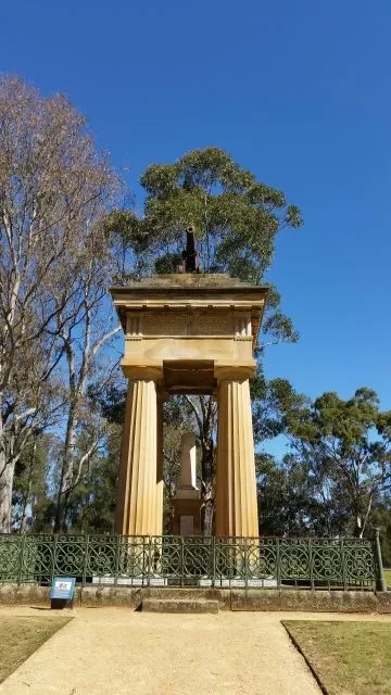 The historic Boer War Memorial featuring classic sandstone columns, a central broken pillar, and a mounted cannon on top, set against a bright blue sky at Parramatta Park.