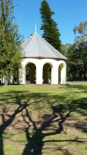 A historic white domed rotunda with arched openings set on a green lawn with tree branch shadows in the foreground at Parramatta Park.