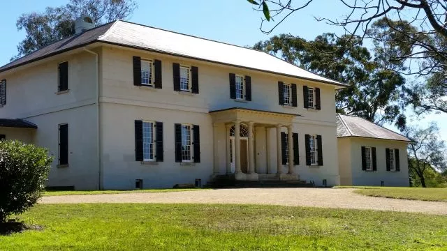 The historic Government House building set amidst the open lawns and mature trees of Parramatta Park under a bright blue sky.
