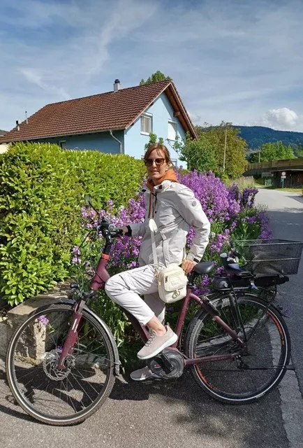 Woman wearing an ivory Wag Society Memory Walk Pouch while cycling through a scenic mountain path in the Austrian countryside near Bregenz.