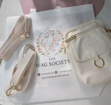 Flat lay of the ivory Wag Society Memory Walk Pouch, two interchangeable straps, and branded packaging.