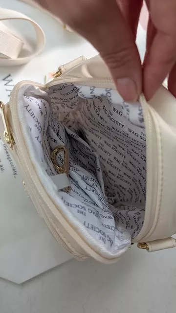 Close-up of the open main compartment of the ivory Wag Society Memory Walk Pouch, showing the branded lining and a gold key clip attachment inside