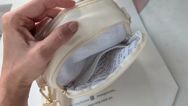 Close-up of the opened main compartment of the ivory Wag Society Memory Walk Pouch, revealing branded interior lining, an internal pocket, and gold hardware attachments.