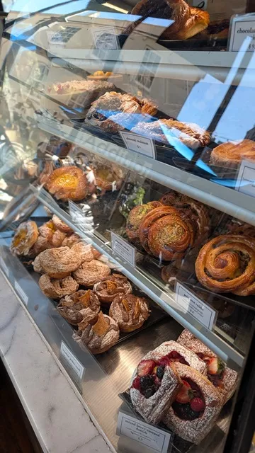 A glass display cabinet packed with artisanal French pastries, croissants, fruit tarts, and danishes at La Renaissance Patisserie.