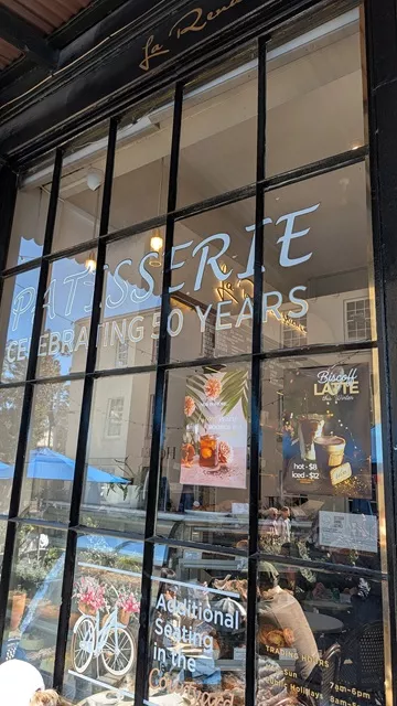 The glass storefront of La Renaissance Patisserie in Sydney with lettering that reads Patisserie Celebrating 50 Years and signs for additional seating.