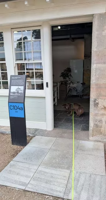 Monte entering through the front door of Havenstone Cafe past an interpretive heritage sign marked C104a.