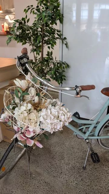A light blue vintage bicycle with a basket full of cream and pink floral arrangements parked inside Havenstone Cafe.