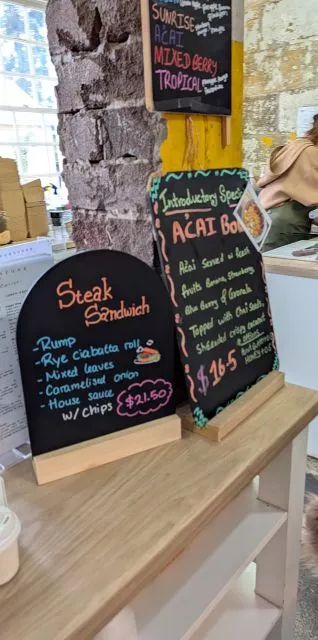 Handwritten chalkboard menus displaying steak sandwich and acai bowl specials on a counter inside Havenstone Cafe.