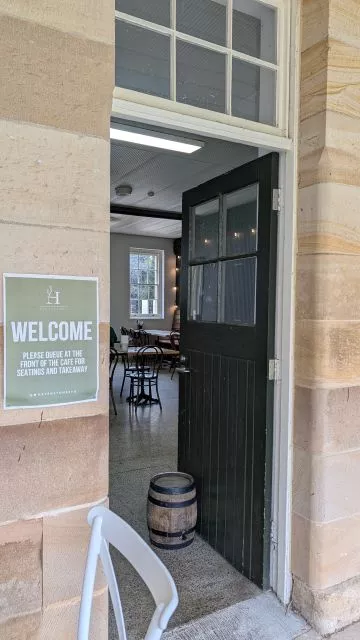 An open dark green door set in a sandstone wall with a welcome sign at the back entrance of Havenstone Cafe.