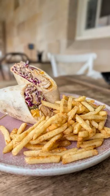 A halved peri peri chicken wrap with fresh slaw and seasoned fries on a pink plate at Havenstone Cafe in Parramatta.