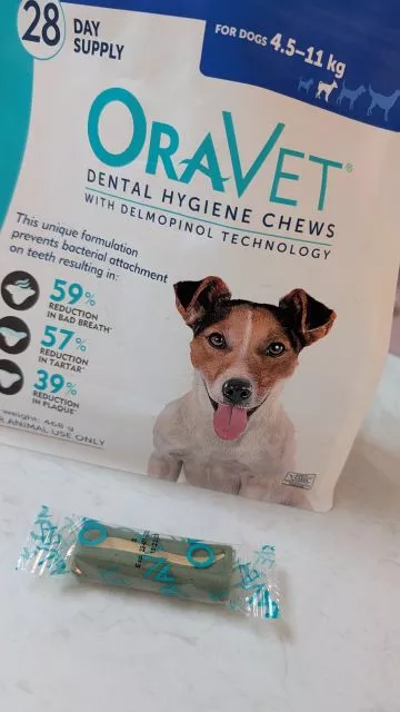 A packet of OraVet Dental Hygiene Chews for small dogs next to a single individually wrapped green chew on a light surface.