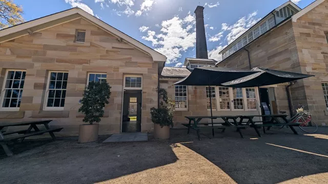 Black picnic tables and large outdoor umbrellas set outside the historic sandstone building and brick chimney at Havenstone Cafe.